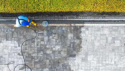 A worker uses a pressure washer to clean a stone patio