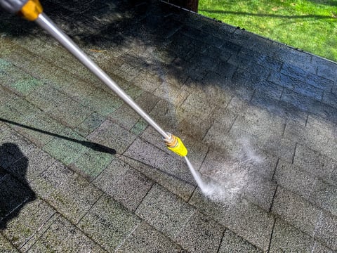 A pressure washer is being used to clean the roof of a house
