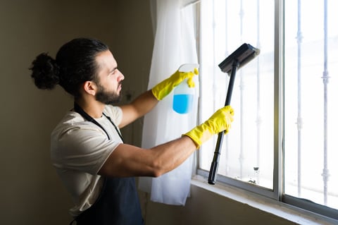 Hispanic cleaner diligently washing windows with cleaning products and gloves