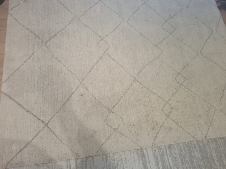 Close-up of beige diamond-patterned carpet with visible wear and dirt marks on the surface