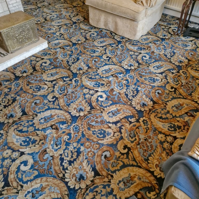 Large ornate area rug with blue and gold damask pattern in living room with beige furniture