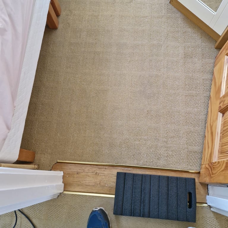 Overhead view of beige carpet in a room with wooden furniture edges and a black door mat on the floor