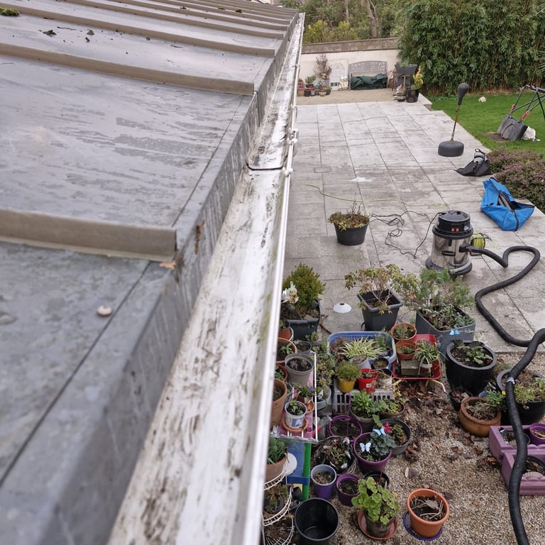 Overhead view of a concrete patio with gardening setup showing potted plants, gardening tools, hose, and patio furniture on grass