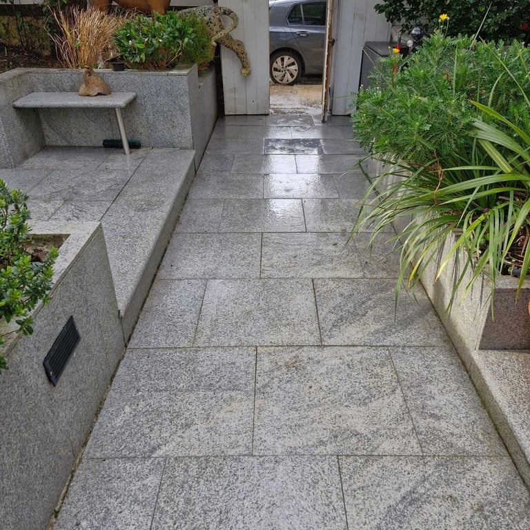 Modern patio pathway with gray stone tiles, flanked by potted plants and stone planters on both sides, leading to parked cars