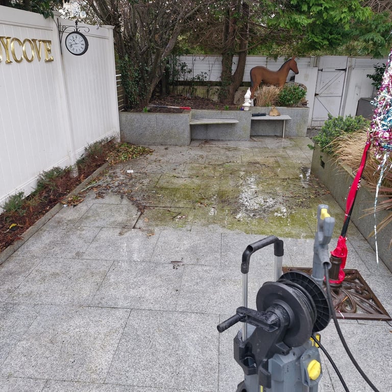 Pressure washing a residential patio surrounded by potted plants, equipment, and an American flag